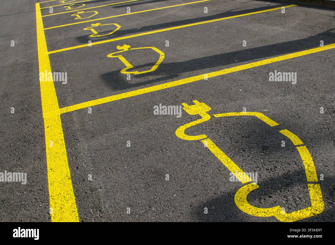 Vista prospettica di una fila di posti auto riservati vuoti per veicoli elettrici. Scatto ad angolo alto di simboli di presa di corrente per auto elettriche dipinti di giallo Foto Stock