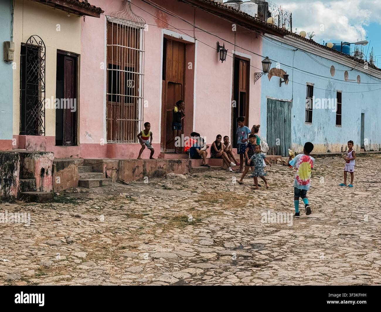 Cuba – 20 dicembre 2024: Vista di bambini che giocano su una strada acciottolata davanti a case colorate in stile coloniale. Foto Stock