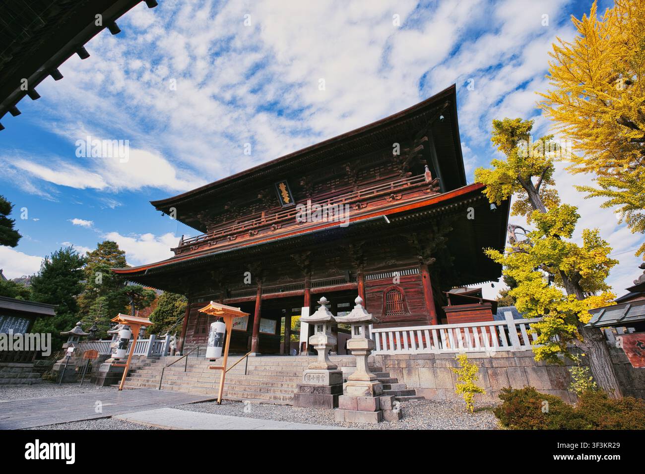 Nagano, Giappone - 06 novembre 2025: Vista del portale del tempio Zenko-ji con architettura tradizionale in legno, lanterne di pietra e vibranti alberi di ginkgo gialli u Foto Stock