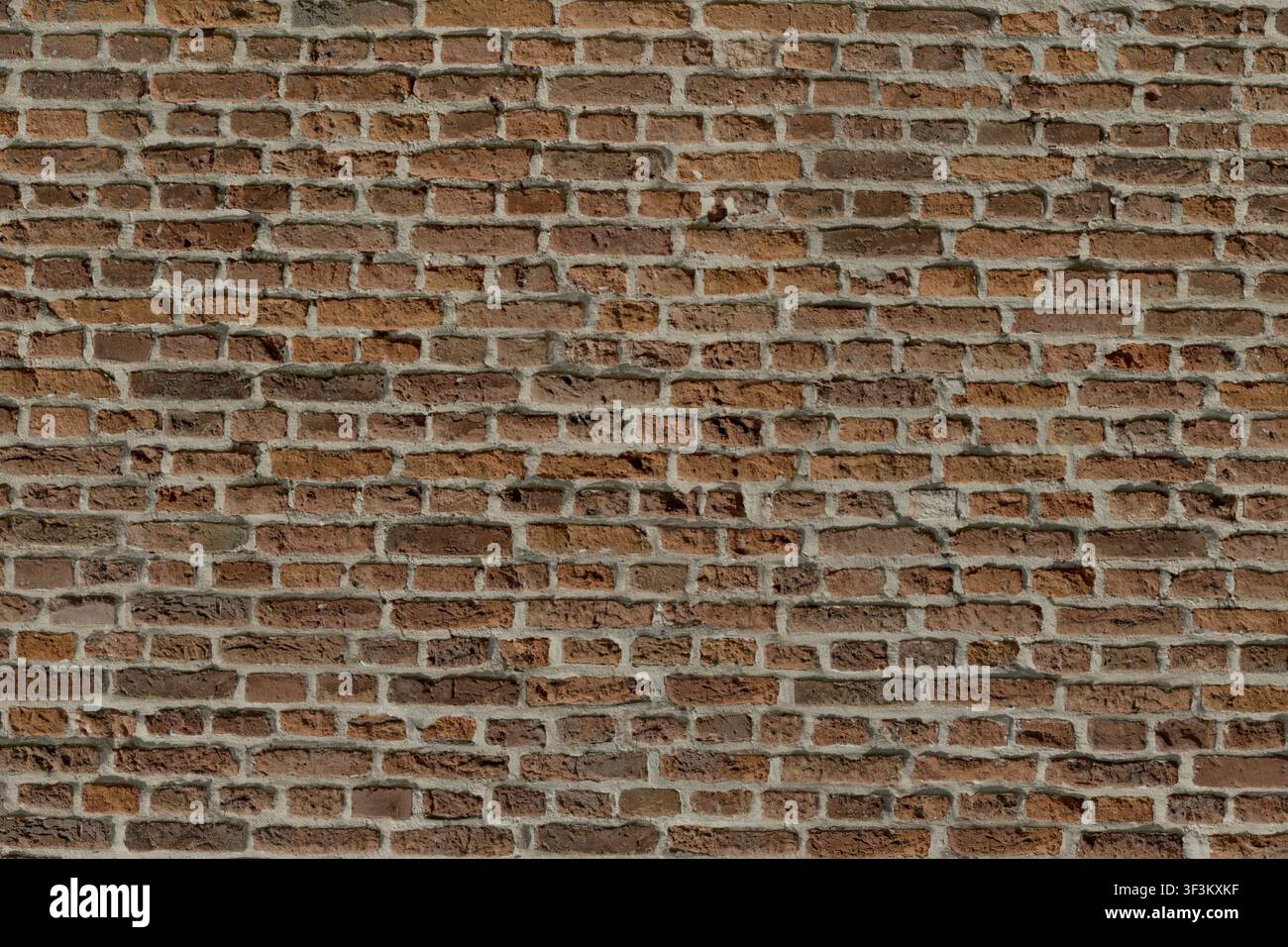 Una sezione di muro esterno di una vecchia chiesa in mattoni, che mostra varie sfumature di mattoni rossi stagionati e linee di malta robuste. Foto Stock