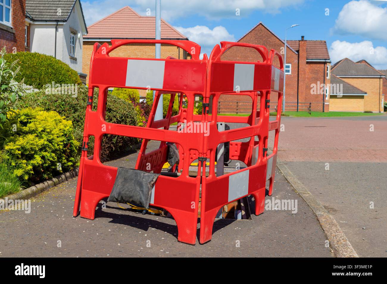 Barriere di sicurezza in plastica interbloccate stile Hannibal rosse che formano un'area di lavoro recintata intorno a una camera di accesso alle telecomunicazioni aperta in un complesso residenziale Foto Stock