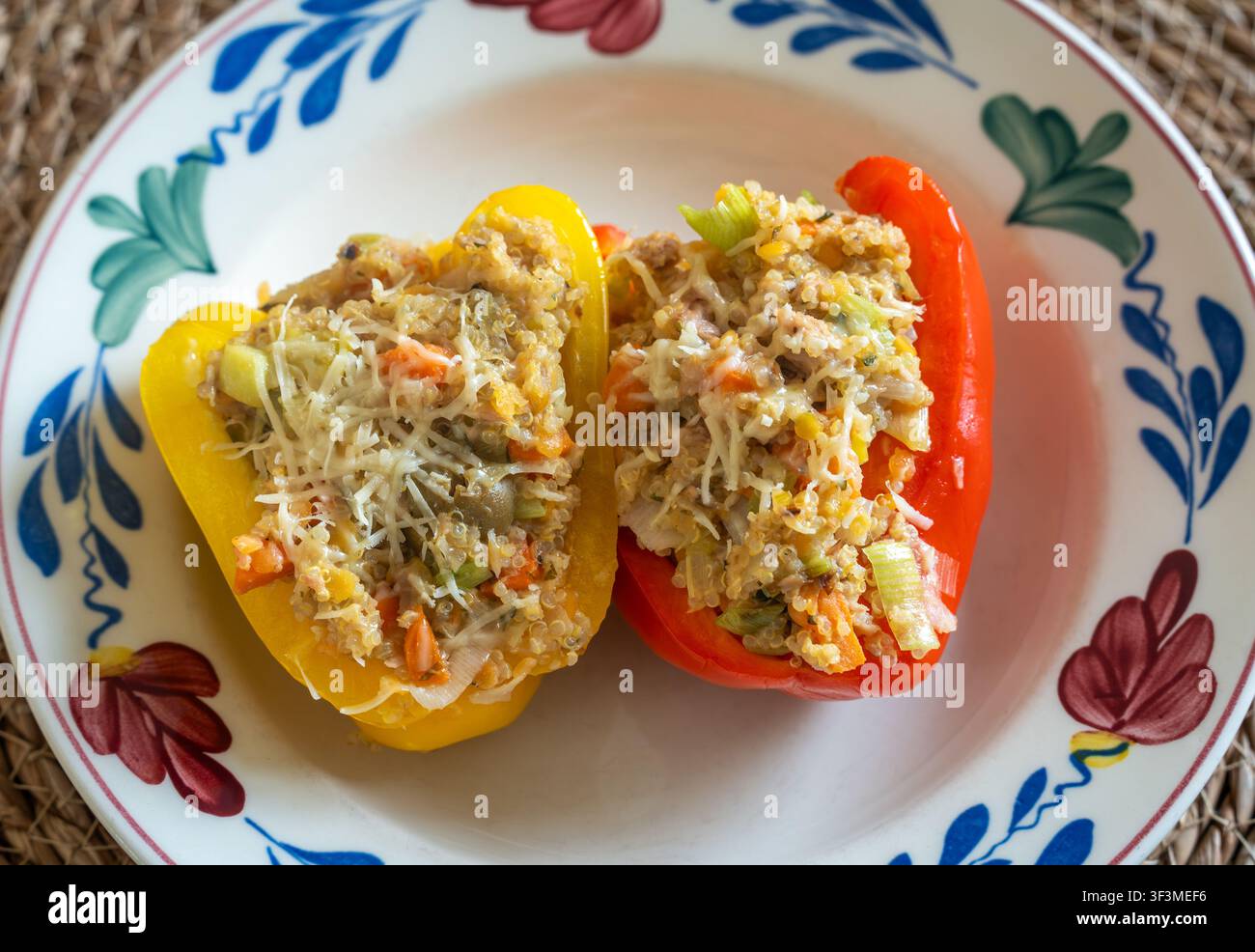 Peperoni ripieni di quinoa cotti al forno, ricoperti di formaggio fuso su un piatto da portata Foto Stock