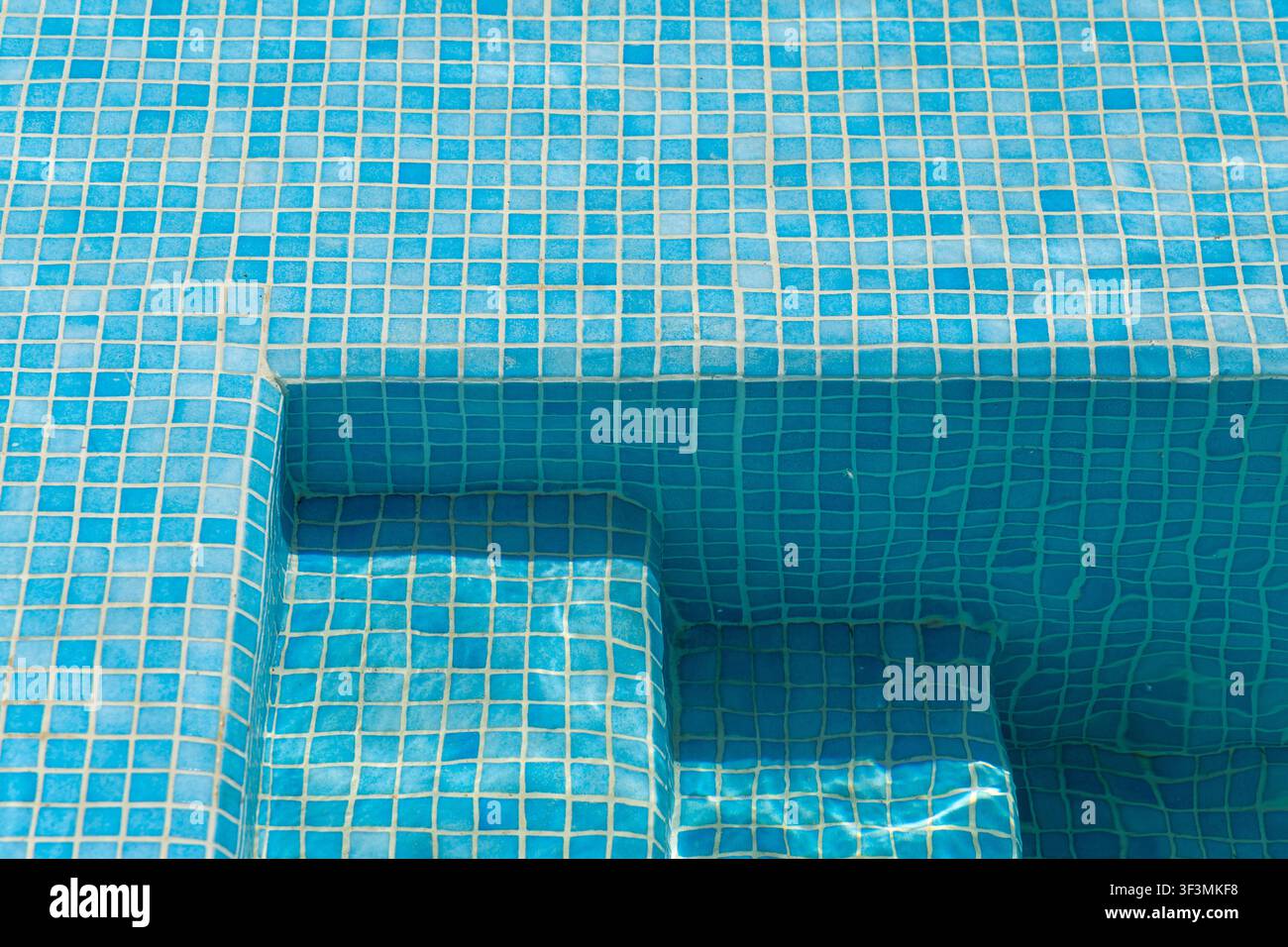 L'intreccio di piccole piastrelle blu forma una superficie ruvida sui gradini e sulle pareti di una piscina immacolata Foto Stock