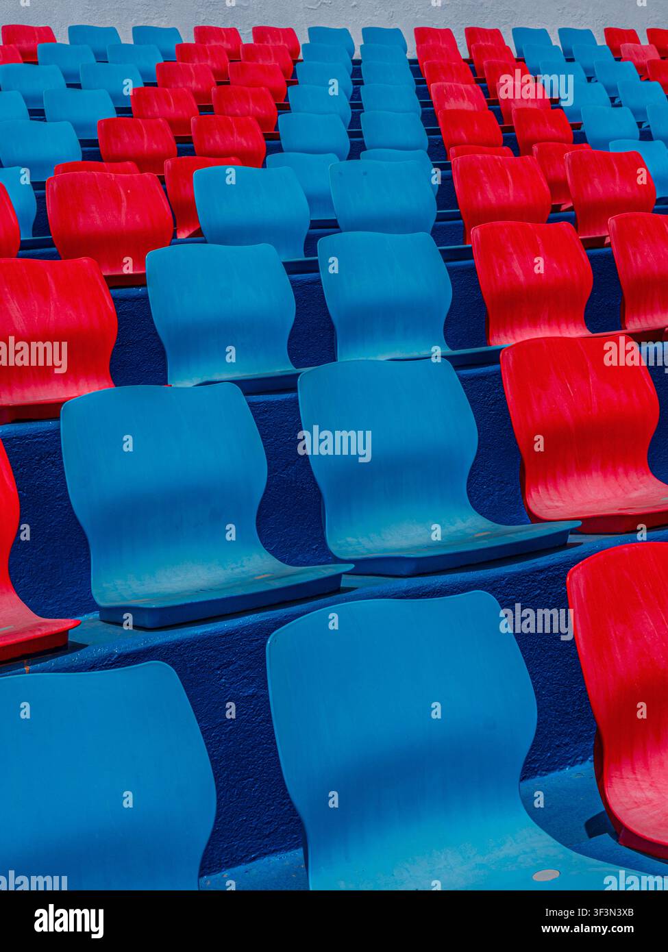 File di sedili di plastica rossi e blu vuoti in uno stadio sportivo all'aperto. Foto Stock