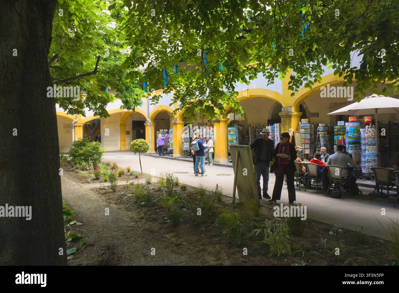 I turisti esplorano negozi di souvenir e caffè all'aperto all'interno del cortile interno dello storico Espace Van Gogh ad Arles, in Francia. Foto Stock