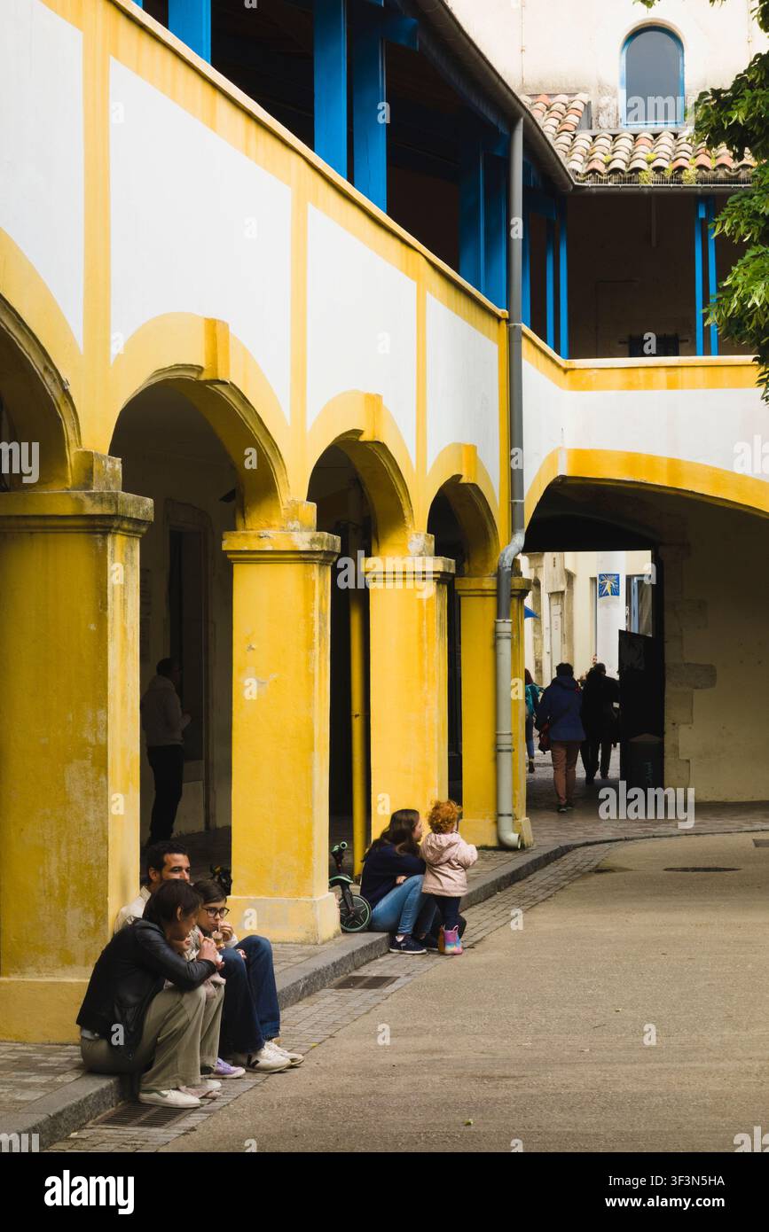 I visitatori sono seduti lungo l'iconica arcata gialla nel centro culturale storico Espace Van Gogh ad Arles, in Francia. Foto Stock