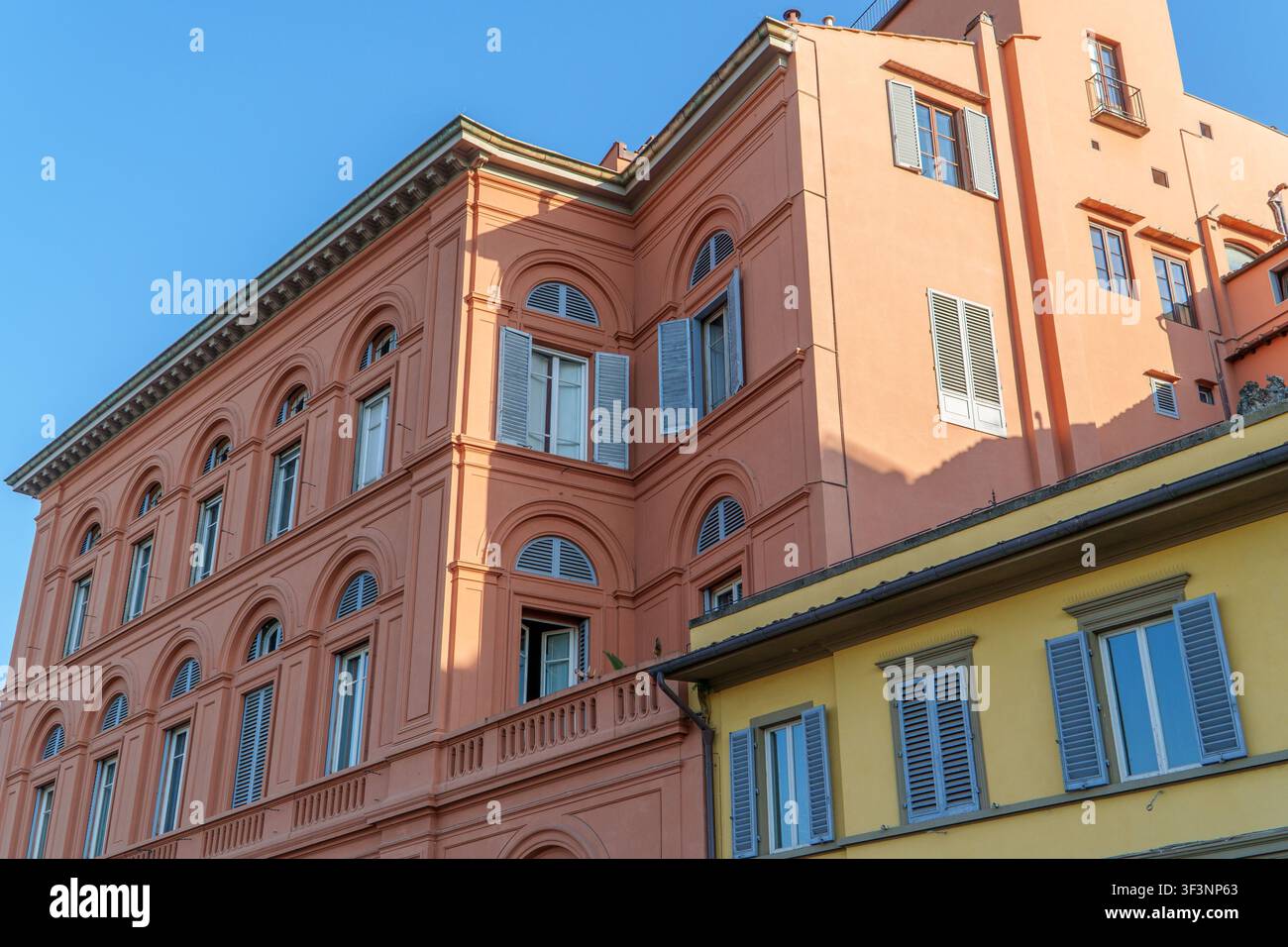La luce del sole illumina bellissimi edifici storici color pesca e giallo con persiane aperte contro un cielo blu chiaro e vivace in Italia. Foto Stock