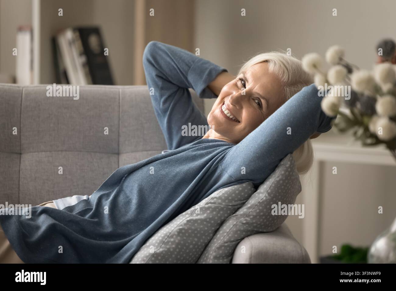 Donna anziana serena sdraiata sul divano con le mani dietro la testa Foto Stock