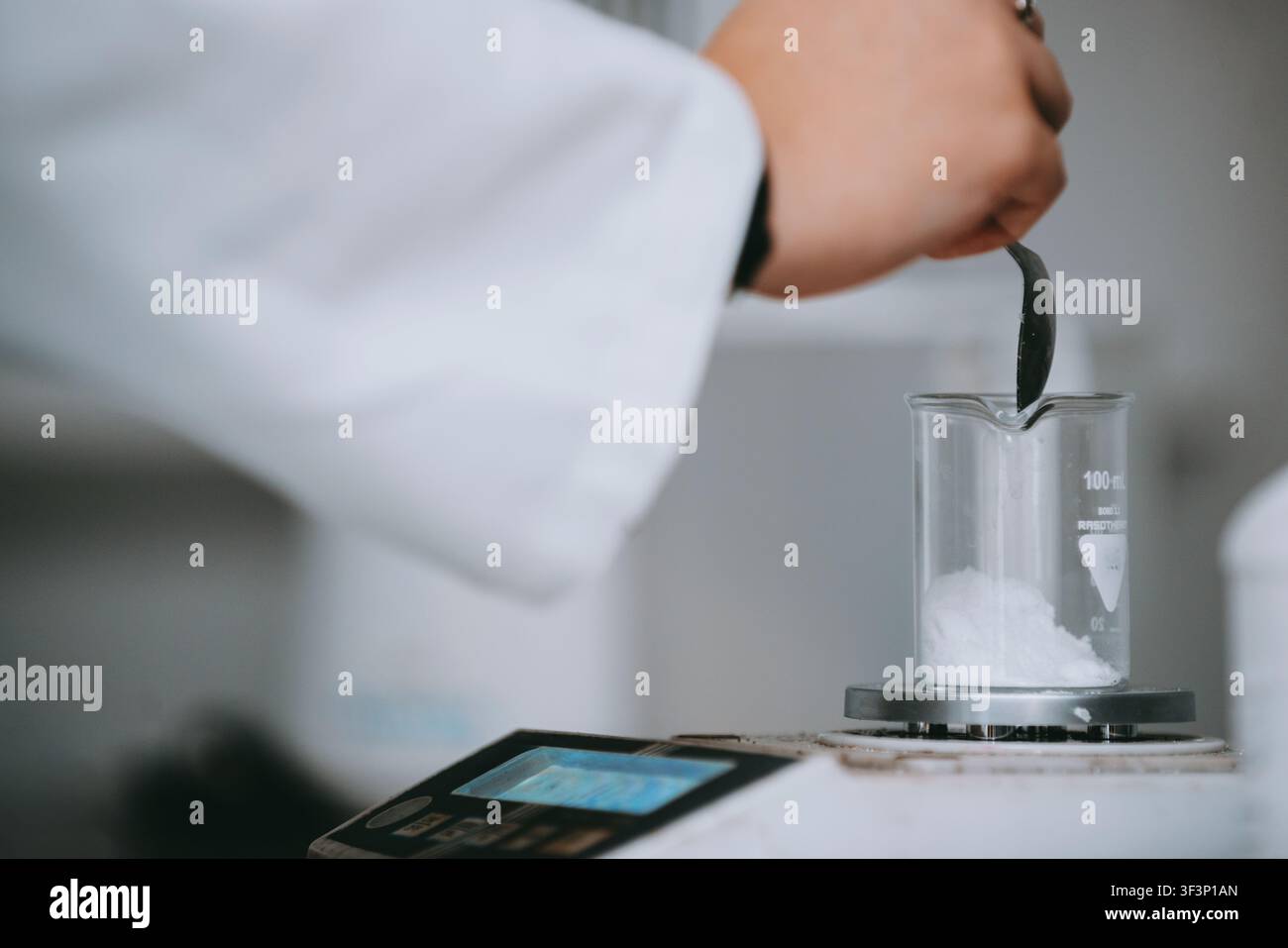 Scienziato di laboratorio che pesa una polvere bianca in un becher di vetro su una bilancia elettronica per l'analisi Foto Stock