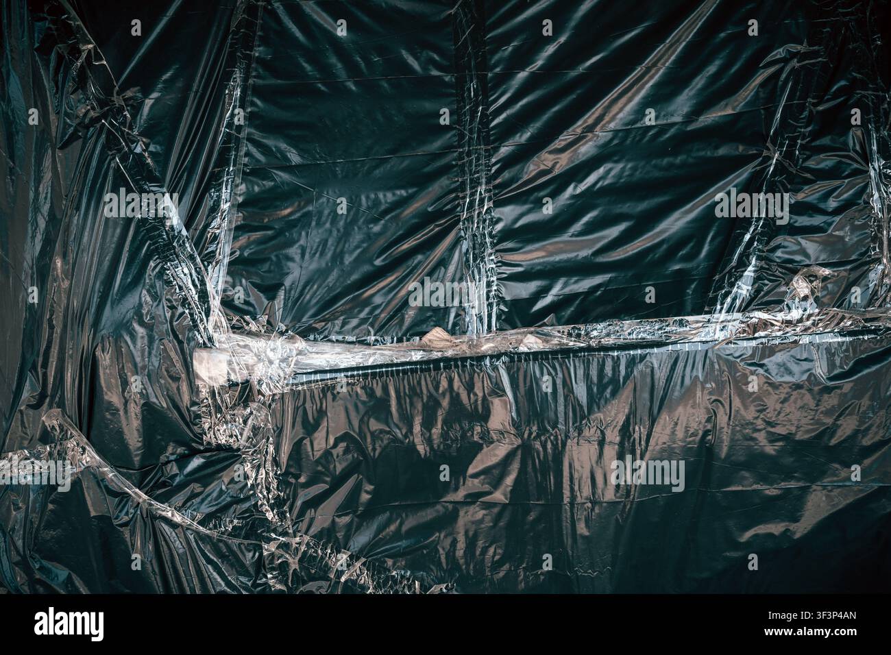 Sfondo in polietilene scuro e lucido che mostra superfici rugose e riflettenti e linee verticali testurizzate. con riflessi drammatici e pieghe Foto Stock