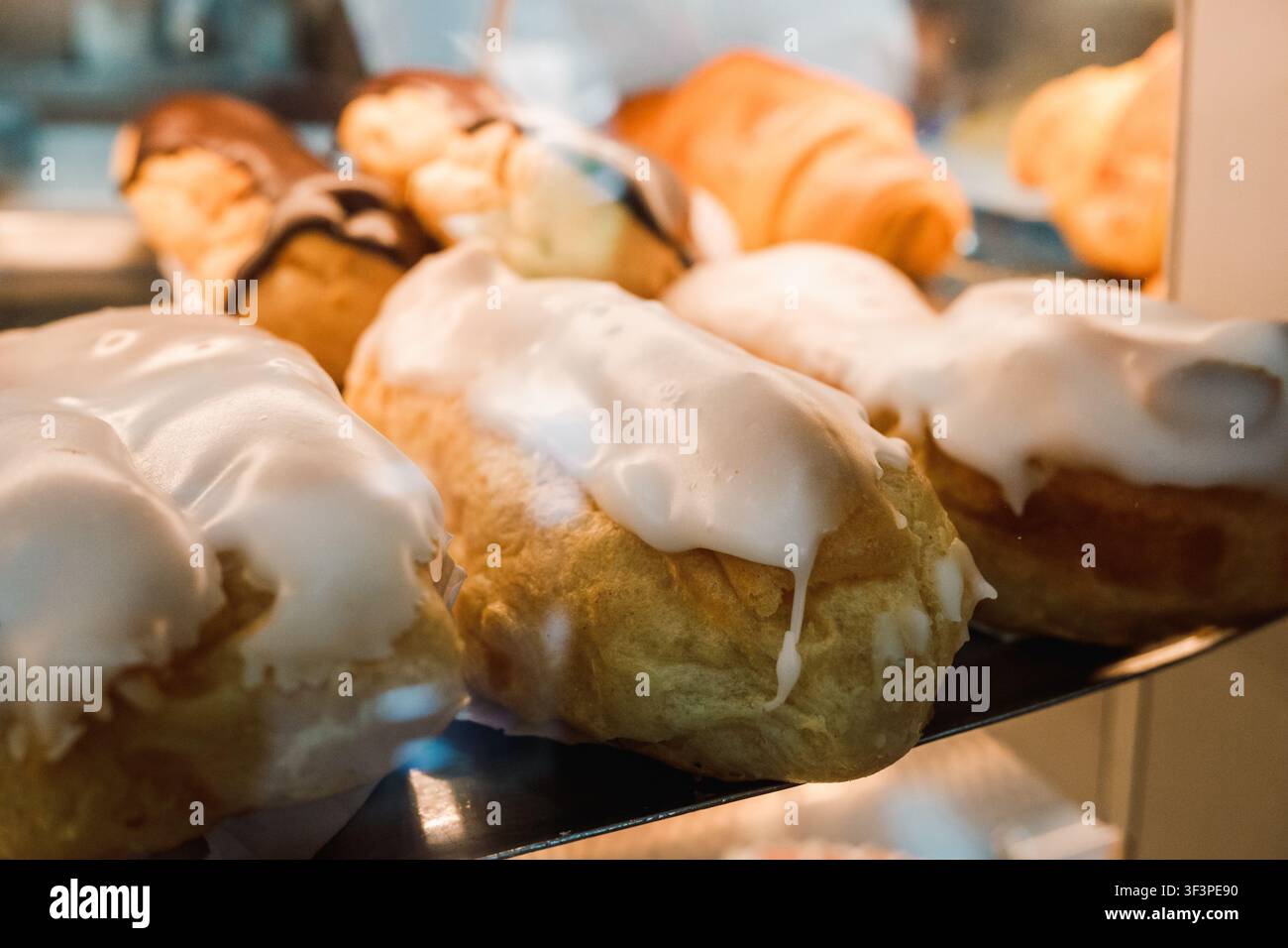 Eclair appena sfornati con glassa alla vaniglia e al cioccolato esposti in una vetrina di pasticceria Foto Stock