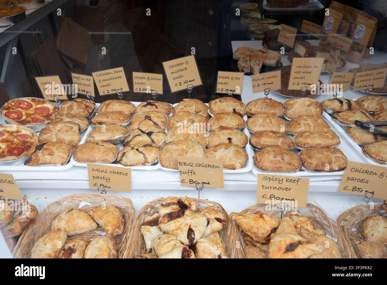 Una vetrina di panetteria piena di torte salate tradizionali, pasticcini e croissant con etichette dei prezzi scritte a mano nel Regno Unito. Foto Stock