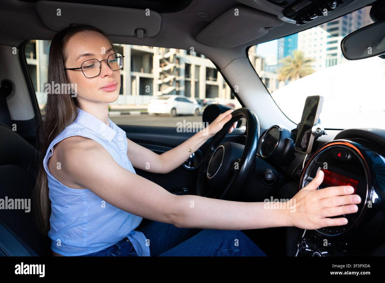 Giovane conducente adulta che sorride mentre tiene il volante in auto durante il giorno Foto Stock