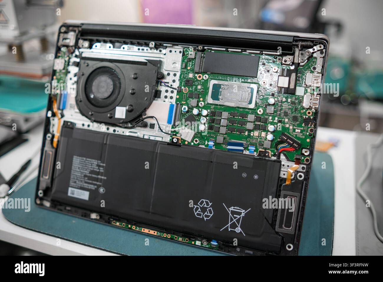 Scheda madre e componenti interni di un laptop esposti su un banco da lavoro, mostrando i dettagli della batteria, della ventola e della scheda elettronica in un contesto di riparazione Foto Stock