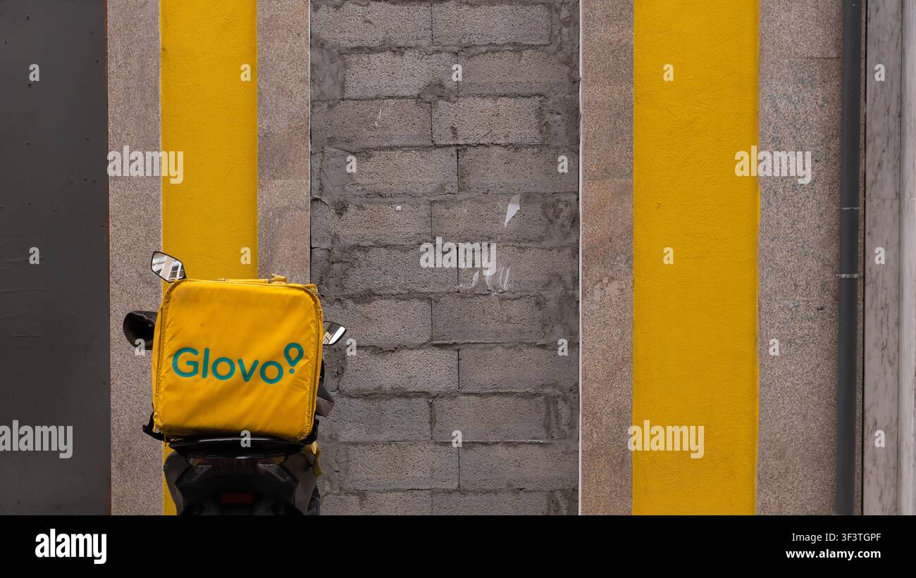 Scooter per consegne Glovo parcheggiato su una strada cittadina – Veicolo da corriere dell’economia gig contro un muro giallo, Porto Portogallo Foto Stock