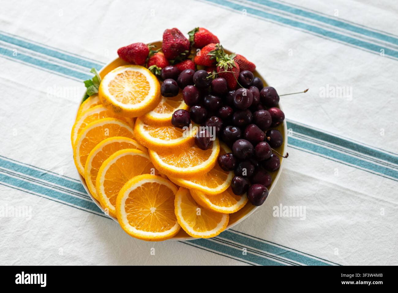 Un vassoio vivace con arance appena tagliate, ciliegie carnose e fragole mature disposte su un panno a righe. Perfetto per uno spuntino rinfrescante Foto Stock