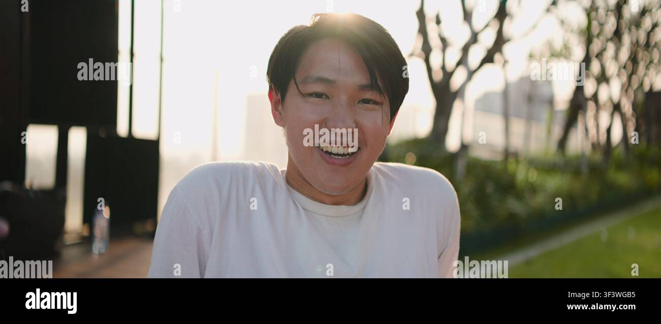 Giovane uomo asiatico che ride con un sorriso raggiante all'aperto all'ora dorata Foto Stock