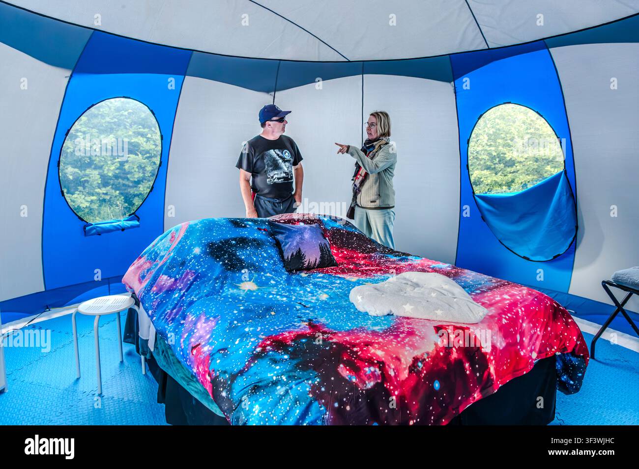 All’interno di una tenda ‘Sky Bubble’ presso l’Osservatorio Deep Sky Eye vicino a Tusket, nella Nuova Scozia, l’ospite Timothy Doucette chiacchiera con Angela Berg davanti al letto, che è rifatto con lenzuola a tema galassia. Finestre trasparenti nella parete della tenda offrono una vista sugli alberi circostanti. Argyle Municipal, Nuova Scozia, Canada Foto Stock