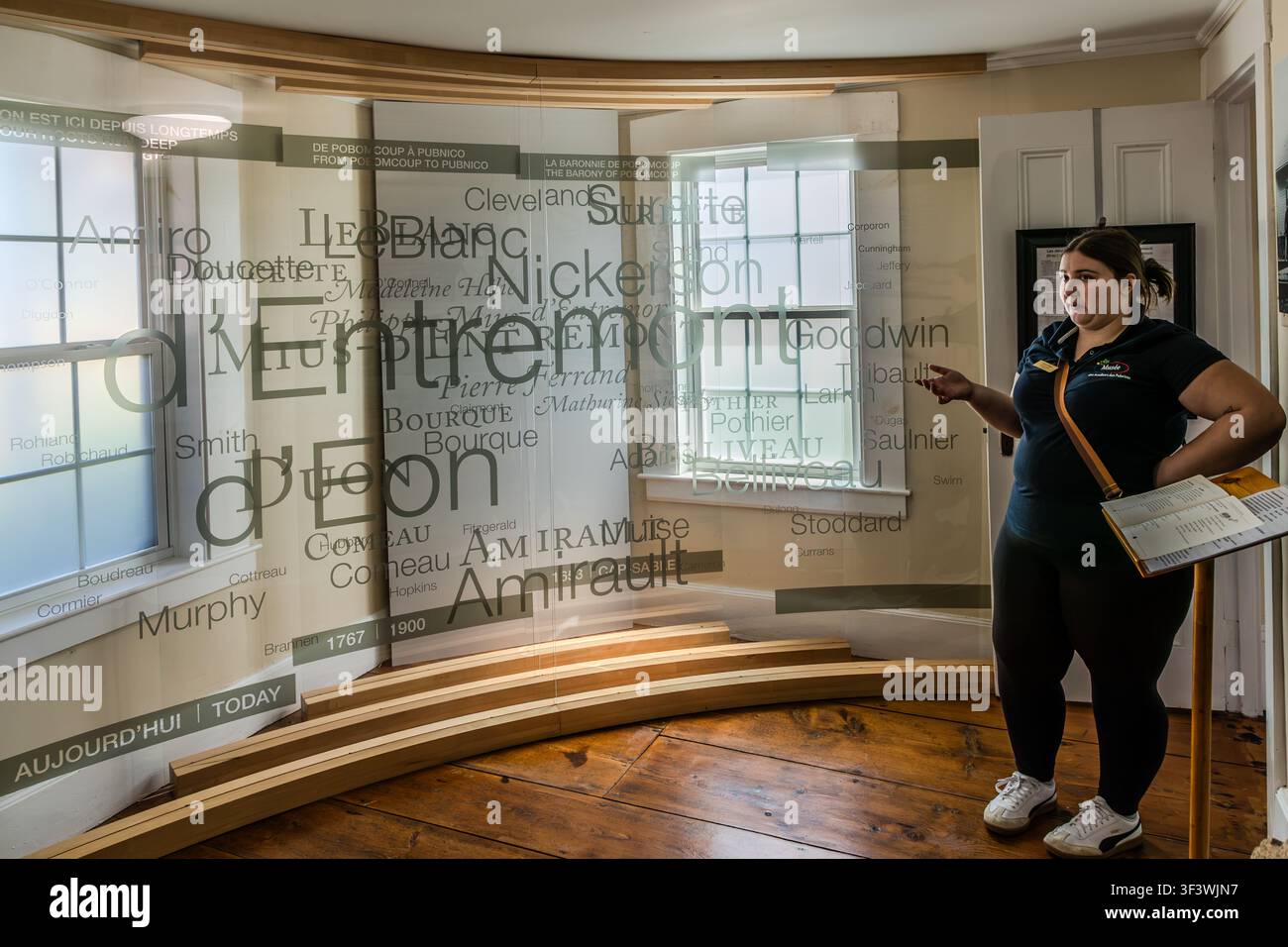 Al Musée des Acadiens des Pubnicos sulla Route 335 a West Pubnico, nella Nuova Scozia, un membro del personale del museo spiega un pannello espositivo che presenta cognomi acadici come d’Entremont, Amirault, LeBlanc e Comeau. L’esposizione, intitolata ‚Da Pobomcoup a Pubnico‘, traccia la storia della Baronia di Pobomcoup – fondata nel 1653 – tra il 1767 e il 1900. Argyle Municipal, Nuova Scozia, Canada Foto Stock