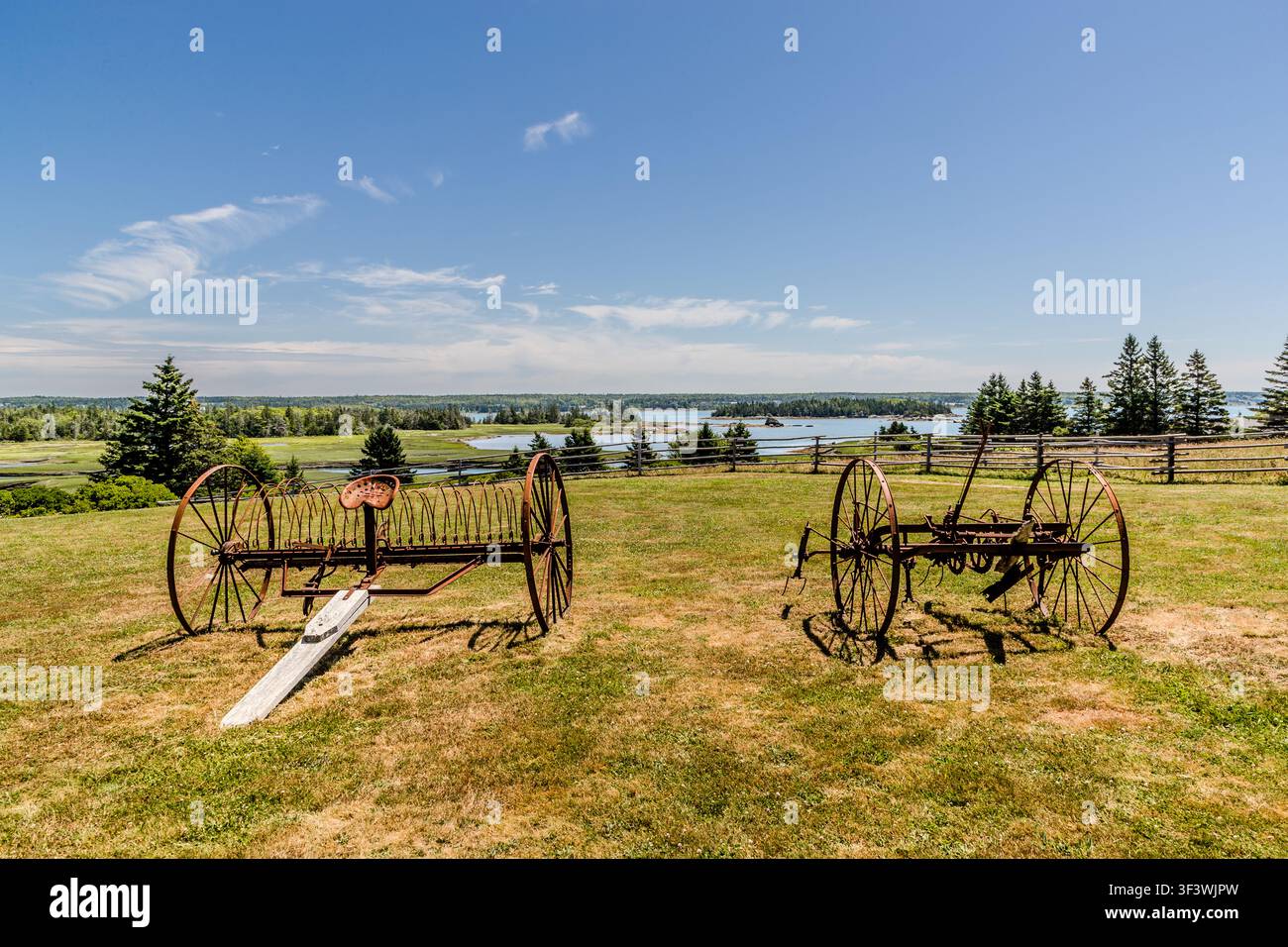 Un rastrello per il fieno e un coltivatore risalenti a circa il 1900 sono in mostra al Le Village historique acadien de la Nouvelle-Écosse su Old Church Road a Lower West Pubnico, Nuova Scozia, con vista sulle isole al largo di Pubnico Harbour. Il museo all'aperto conserva macchine agricole storiche come parte della storia agricola acadiana. Argyle Municipal, Nuova Scozia, Canada Foto Stock