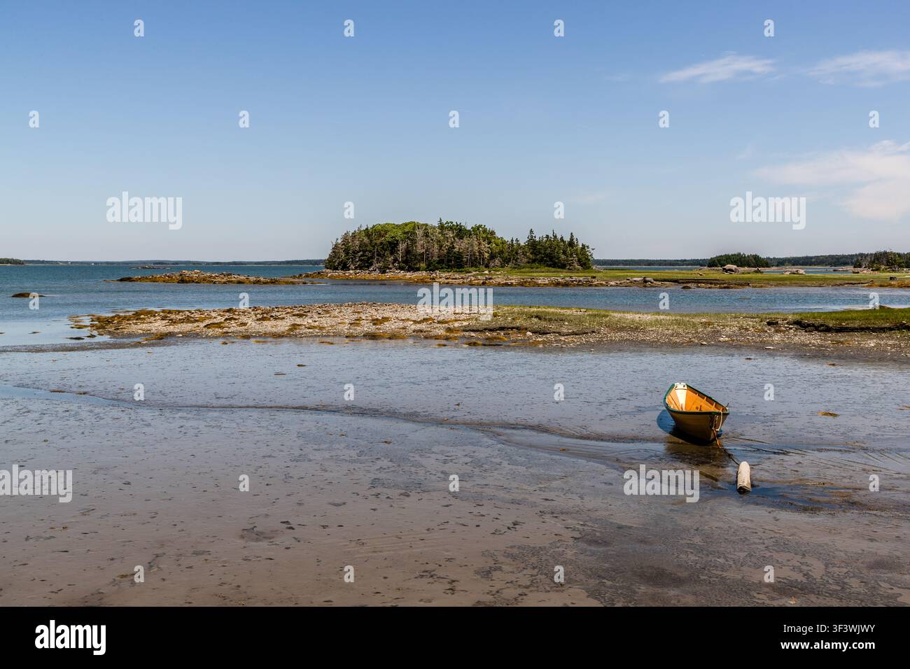 Con la marea bassa, una barca a remi arancione giace sui bassifondi esposti al largo di un'isola boschiva nel porto di Pubnico, vicino a Lower West Pubnico, nella Nuova Scozia. Argyle Municipal, Nuova Scozia, Canada Foto Stock