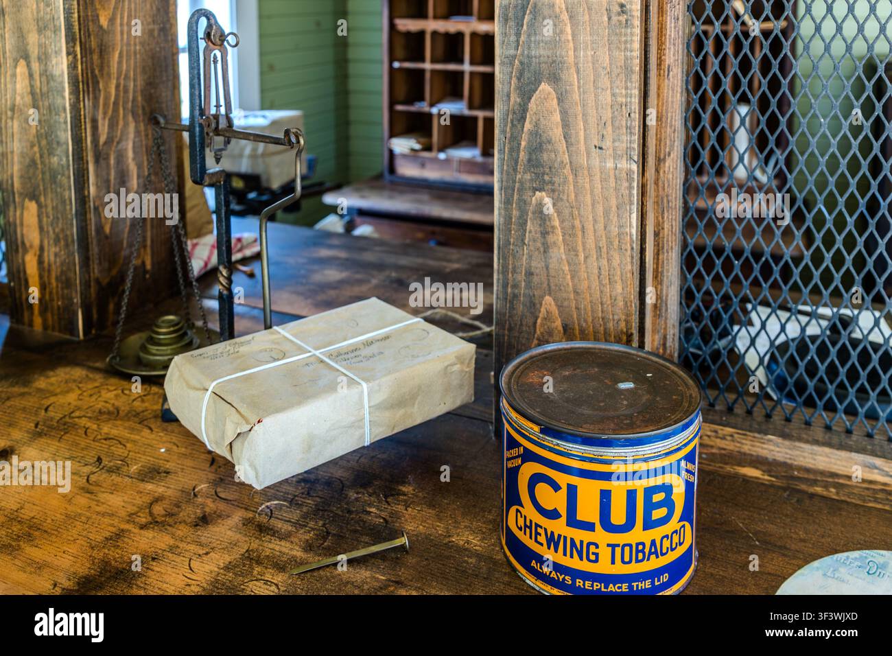 Un pacchetto legato con uno spago giace accanto a un vecchio set di bilance e a una lattina di ‚Club Chewing Tobacco‘ sul bancone della replica dell'edificio postale al Le Village historique acadien de la Nouvelle-Écosse su Old Church Road a Lower West Pubnico, Nova Scotia. In secondo piano si vede il rack di legno delle cassette postali del ‚Bureau de Poste‘ storico. Argyle Municipal, Nova Scotia, Canada Foto Stock