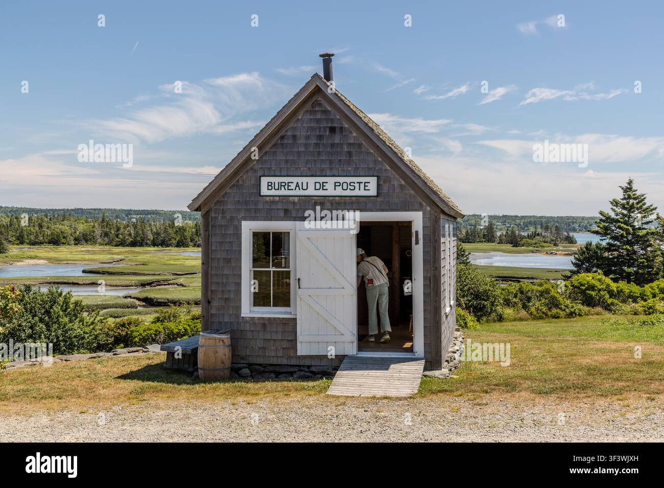 Una persona entra nell’edificio replica dell’ufficio postale, il ‚Bureau de Poste‘, al Villaggio Storico Accadico della Nuova Scozia su Old Church Road a Lower West Pubnico, Nuova Scozia. Il piccolo edificio rivestito di scandole, che si affaccia sulle paludi salate di Pubnico Harbour, raffigura il funzionamento di un ufficio postale rurale intorno al 1900. Argyle Municipal, Nuova Scozia, Canada Foto Stock