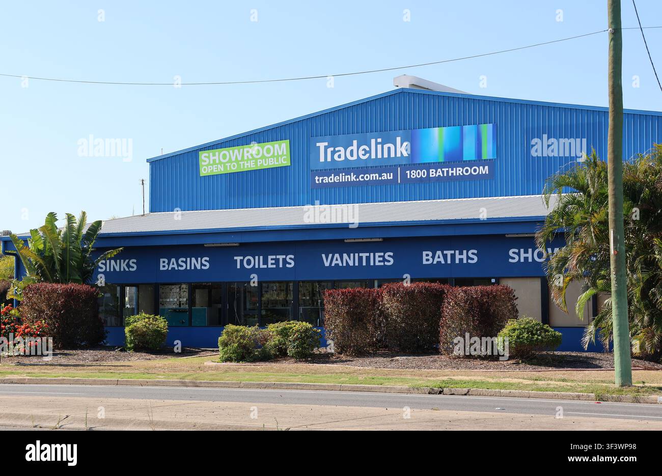 Esterno di un edificio magazzino showroom blu di Tradelink per idraulica con giardino paesaggistico sotto un cielo sereno a Gladstone, Queensland, Australia Foto Stock