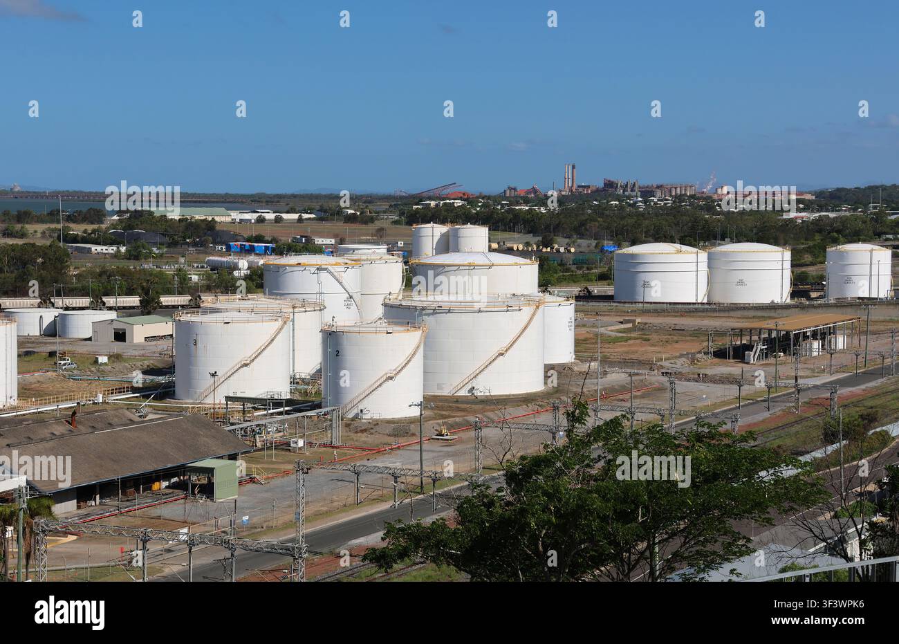 Grandi serbatoi di carburante bianchi si raggruppano in una struttura portuale industriale sotto un cielo blu terso a Gladstone, Queensland, Australia Foto Stock
