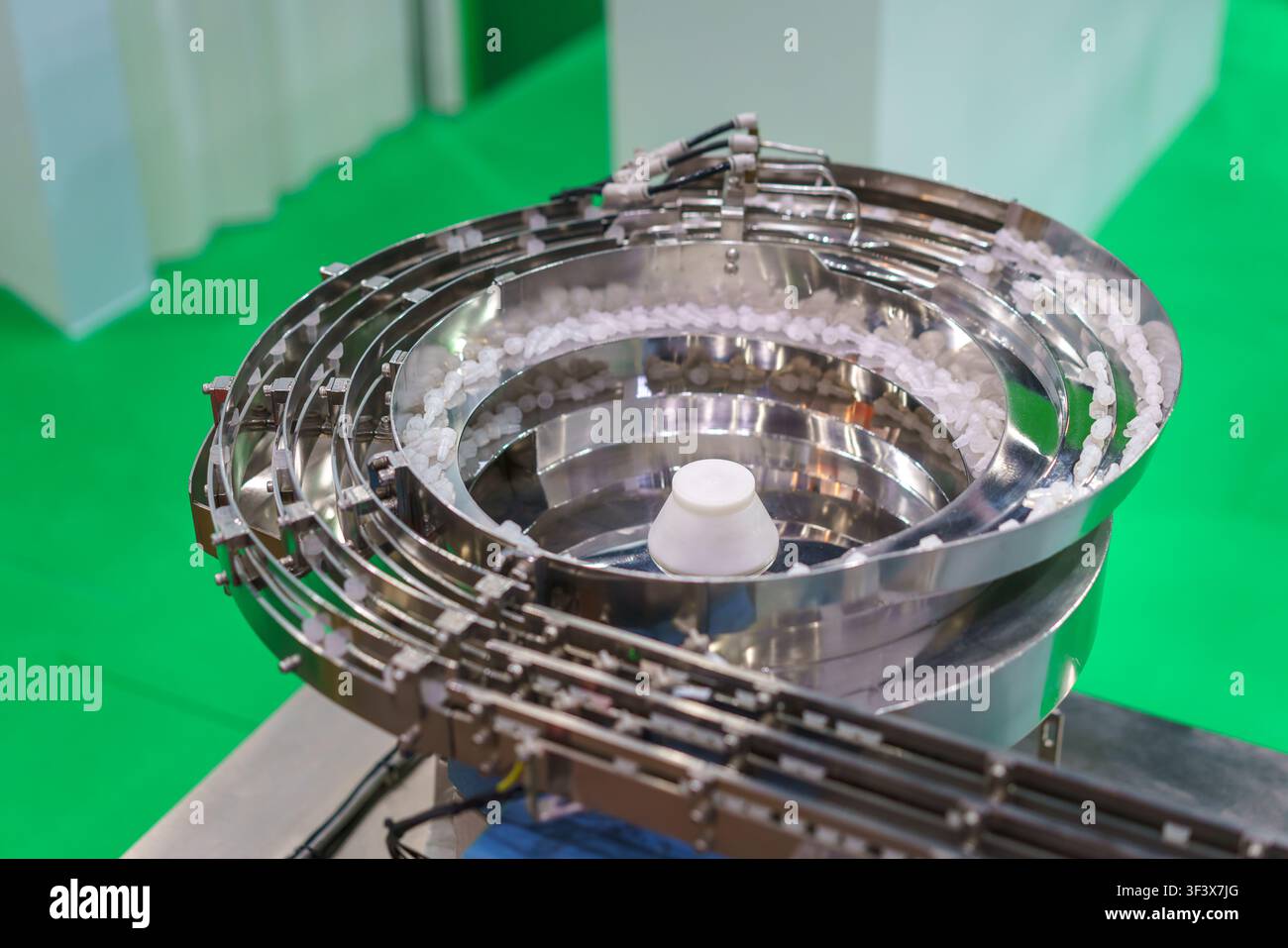 Un alimentatore vibrante in acciaio inossidabile che smista piccoli componenti di plastica bianca su una linea di produzione industriale, evidenziando l'efficienza nell'automazione Foto Stock