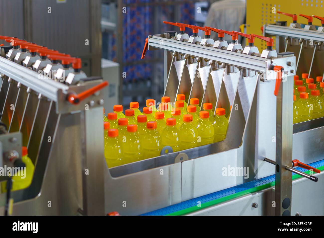 Macchina industriale automatica che smista bottiglie di plastica riempite con liquido giallo e tappi arancioni su un nastro trasportatore in una moderna fabbrica di bevande Foto Stock