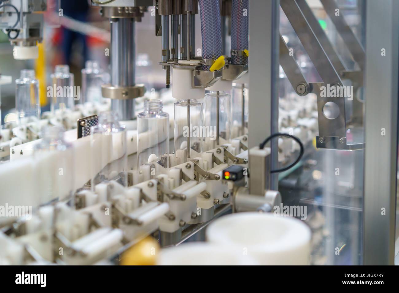 Primo piano di una macchina industriale automatizzata che elabora bottiglie di plastica trasparente su una linea di produzione moderna. L'attrezzatura utilizza ugelli precisi Foto Stock