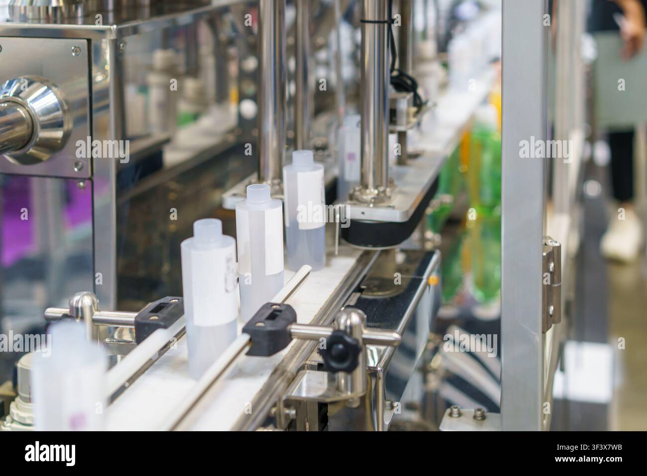 Primo piano di bottiglie di plastica bianca che si muovono lungo un nastro trasportatore in acciaio inossidabile su una macchina automatica per il riempimento e l'imballaggio industriale in una moderna fa Foto Stock