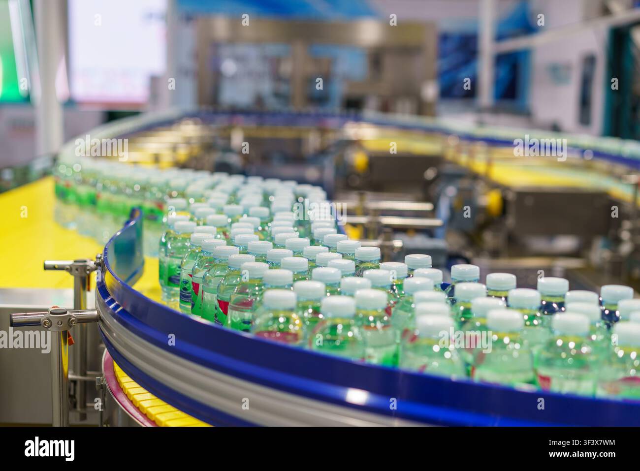 Centinaia di bottiglie di plastica trasparente piene di acqua potabile fresca che si muovono su un nastro trasportatore curvo su una linea di produzione automatizzata all'interno di un moderno Foto Stock