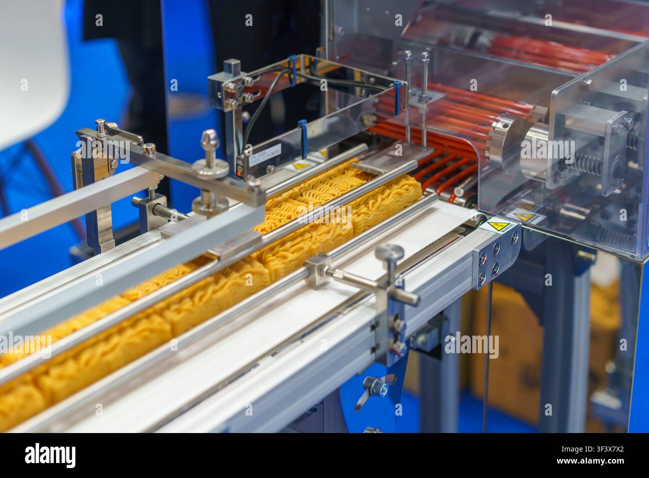 Blocchi di noodles istantanei essiccati che avanzano su un nastro trasportatore attraverso una macchina di confezionamento automatizzata in un moderno stabilimento di produzione alimentare. Foto Stock