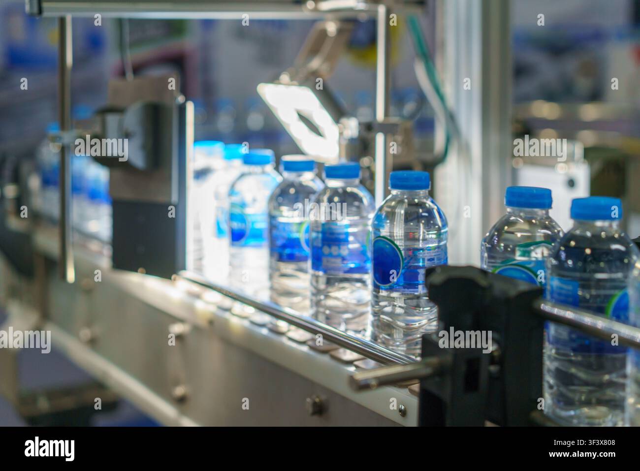 Prima piano di una macchina per l'etichettatura automatica che applica etichette di carta bianca su bottiglie di plastica che avanzano su un nastro trasportatore in un moderno stabilimento di produzione. Foto Stock