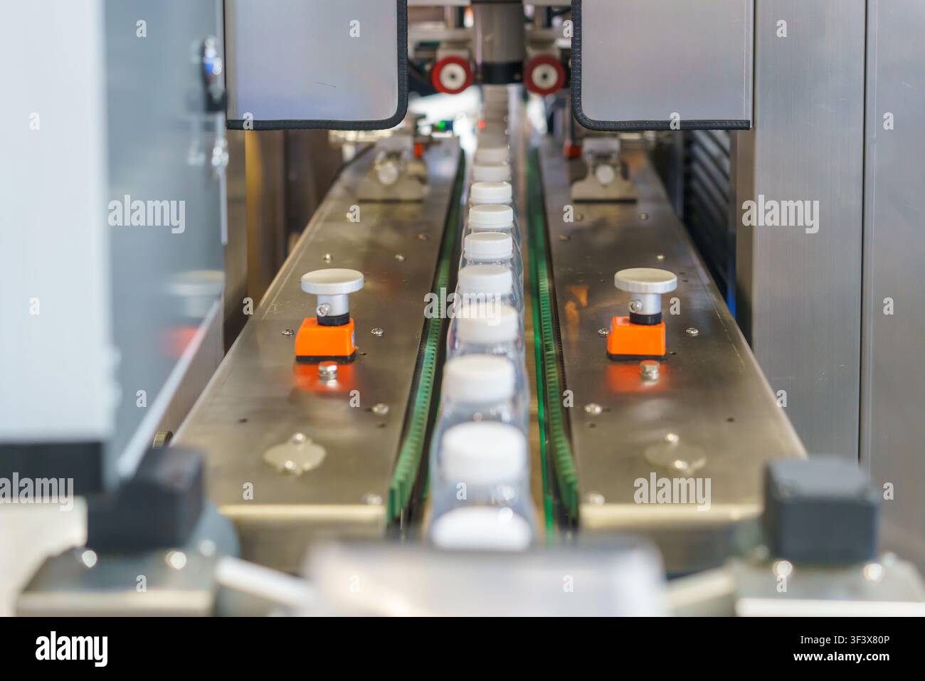 Bottiglie di plastica trasparenti vuote con tappi bianchi che avanzano su un nastro trasportatore in acciaio inossidabile all'interno di uno stabilimento di produzione industriale automatizzato. Foto Stock