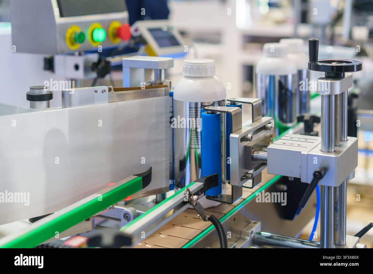 Prima piano di una macchina per l'etichettatura automatica che applica etichette di carta bianca su bottiglie di plastica che avanzano su un nastro trasportatore in un moderno stabilimento di produzione. Foto Stock