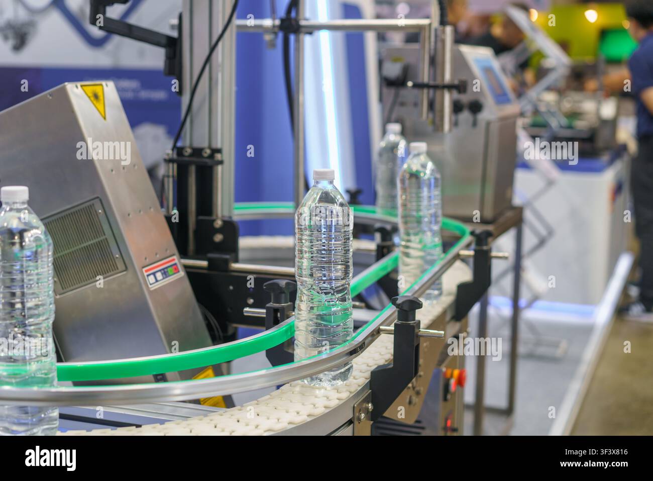 linea di produzione automatizzata con bottiglie d'acqua di plastica. Un sistema di visione artificiale con una luce intensa ispeziona una bottiglia per il controllo qualità in una fabbrica Foto Stock