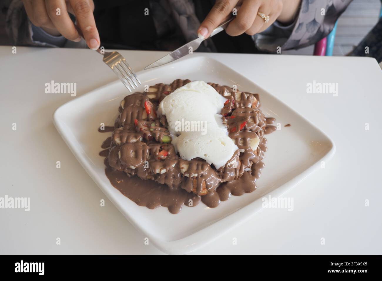 Una persona si gode una waffle ricoperta di salsa al cioccolato e fragole a fette. Foto Stock