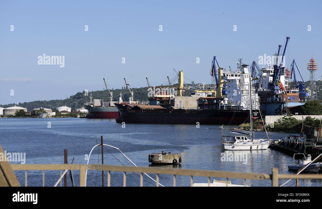Scena portuale industriale con diverse grandi navi, gru e navi commerciali che lavorano sotto un cielo blu terso. Bulgaria, Varna 23 luglio 2026 Foto Stock