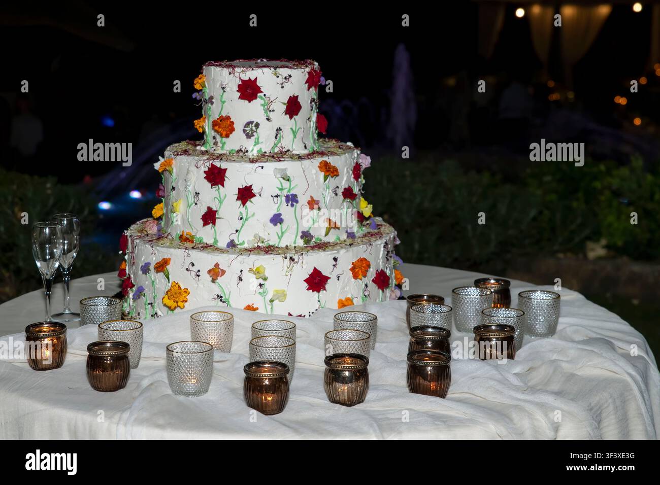 Un grande torta a tre piani decorata con fiori colorati, candele e bicchieri di champagne Foto Stock