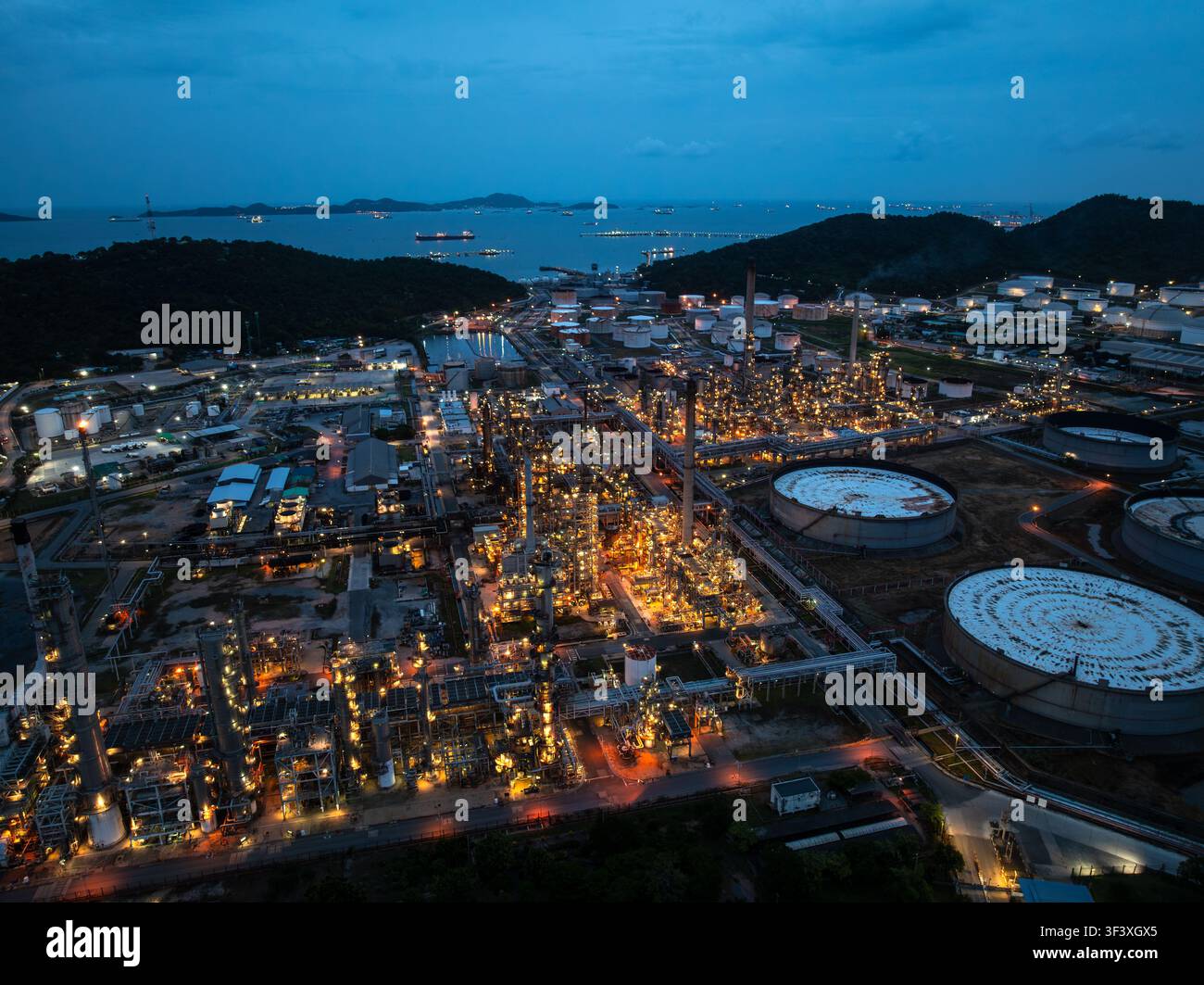 Vista ad angolo alto della sera di un complesso di raffineria petrolchimica illuminato con serbatoi lungo la costa a Si Racha, Chonburi, Thailandia Foto Stock