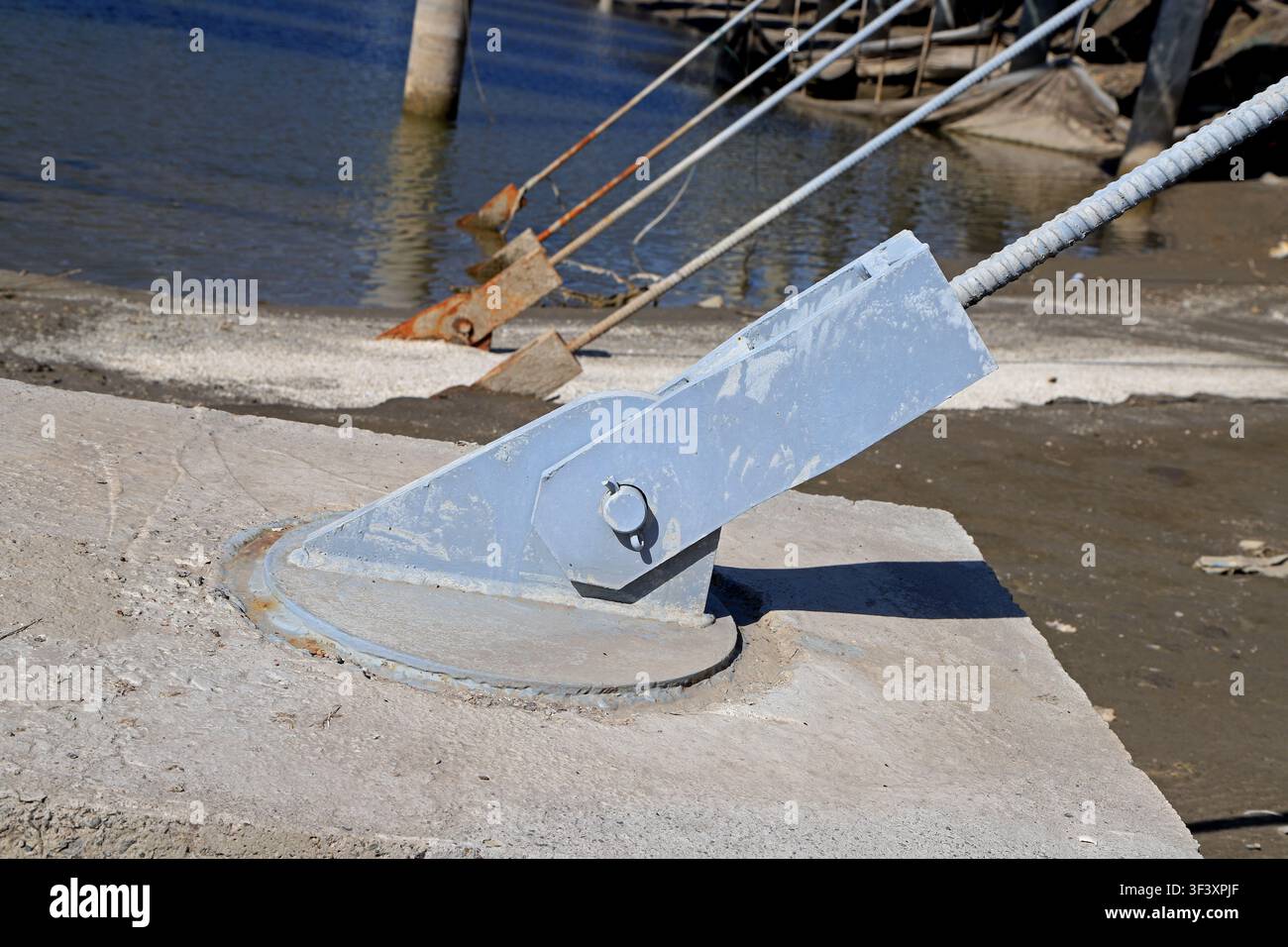 L'immagine mostra componenti di ancoraggio in metallo blu e arrugginiti di una centrale fotovoltaica galleggiante, fissati su basi di cemento e collegati all'acciaio Foto Stock