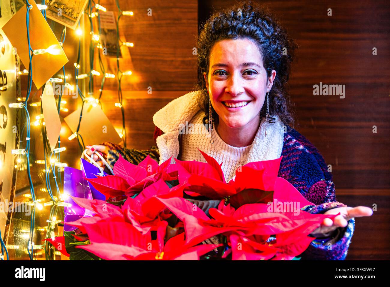 Giovane donna che si gode la stagione delle festività con una pianta di poinsettia Foto Stock