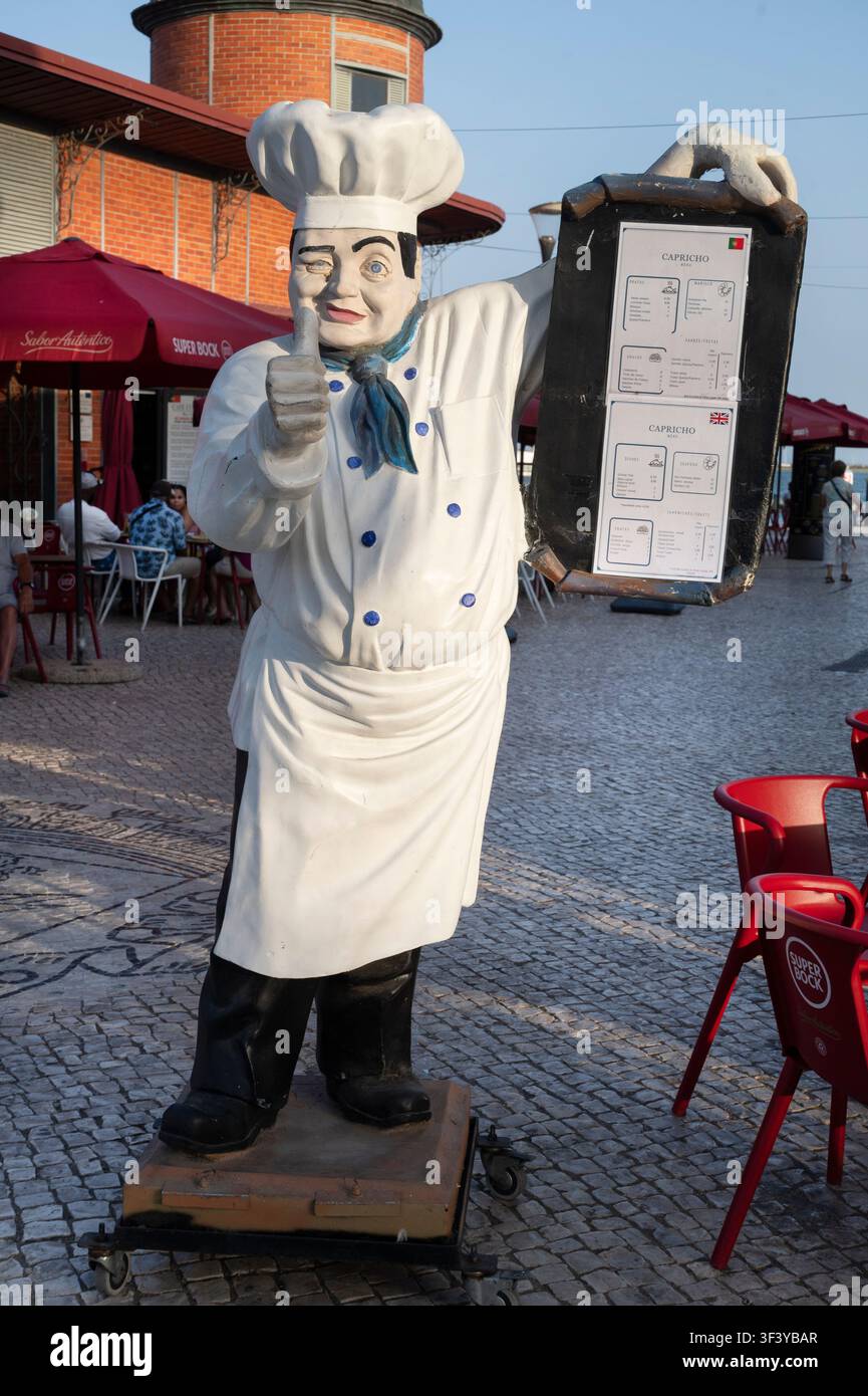 Luglio 2026 Portogallo. Olhão. Modello in plastica di uno chef che tiene un menù davanti a un caffè Foto Stock