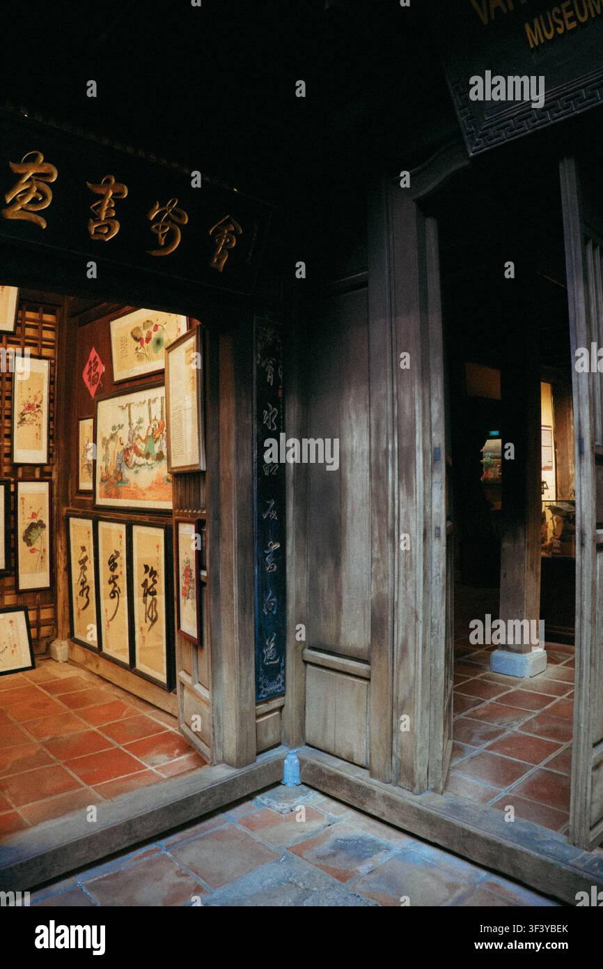 Hoi An, Vietnam, 1 luglio 2026. Un ingresso storico in legno scuro mostra dipinti su rotoli cinesi tradizionali e targhe dorate con iscrizioni sopra un patte Foto Stock