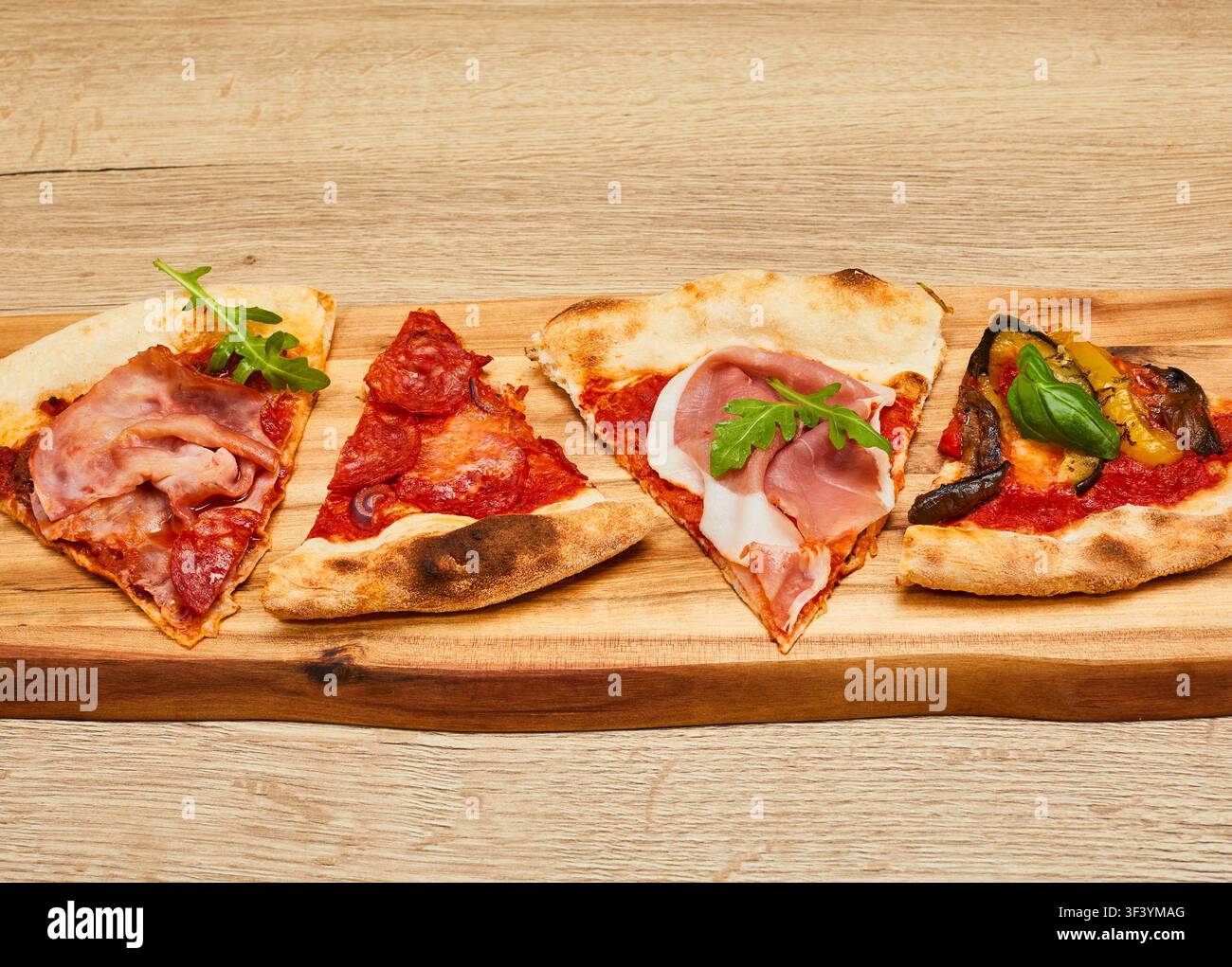 Quattro fette di pizza diverse con vari condimenti servite su una tavola di legno posizionata su uno sfondo di tavolo in legno. Foto Stock