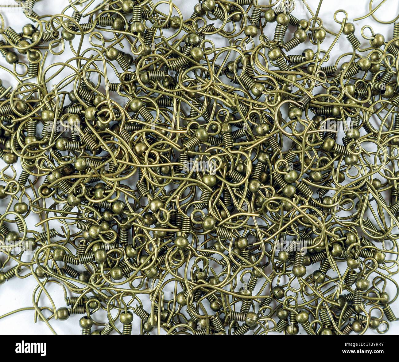 Numerosi ganci per orecchini in tono bronzo sono disposti in modo intricato, mostrando una varietà di forme e dimensioni ideali per la creazione di gioielli. Questi ganci offrono versatilità Foto Stock
