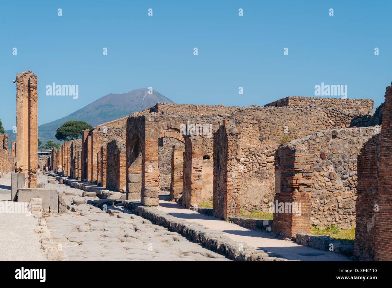 Turisti che camminano tra le rovine archeologiche di Pompei con il Vesuvio sullo sfondo Foto Stock